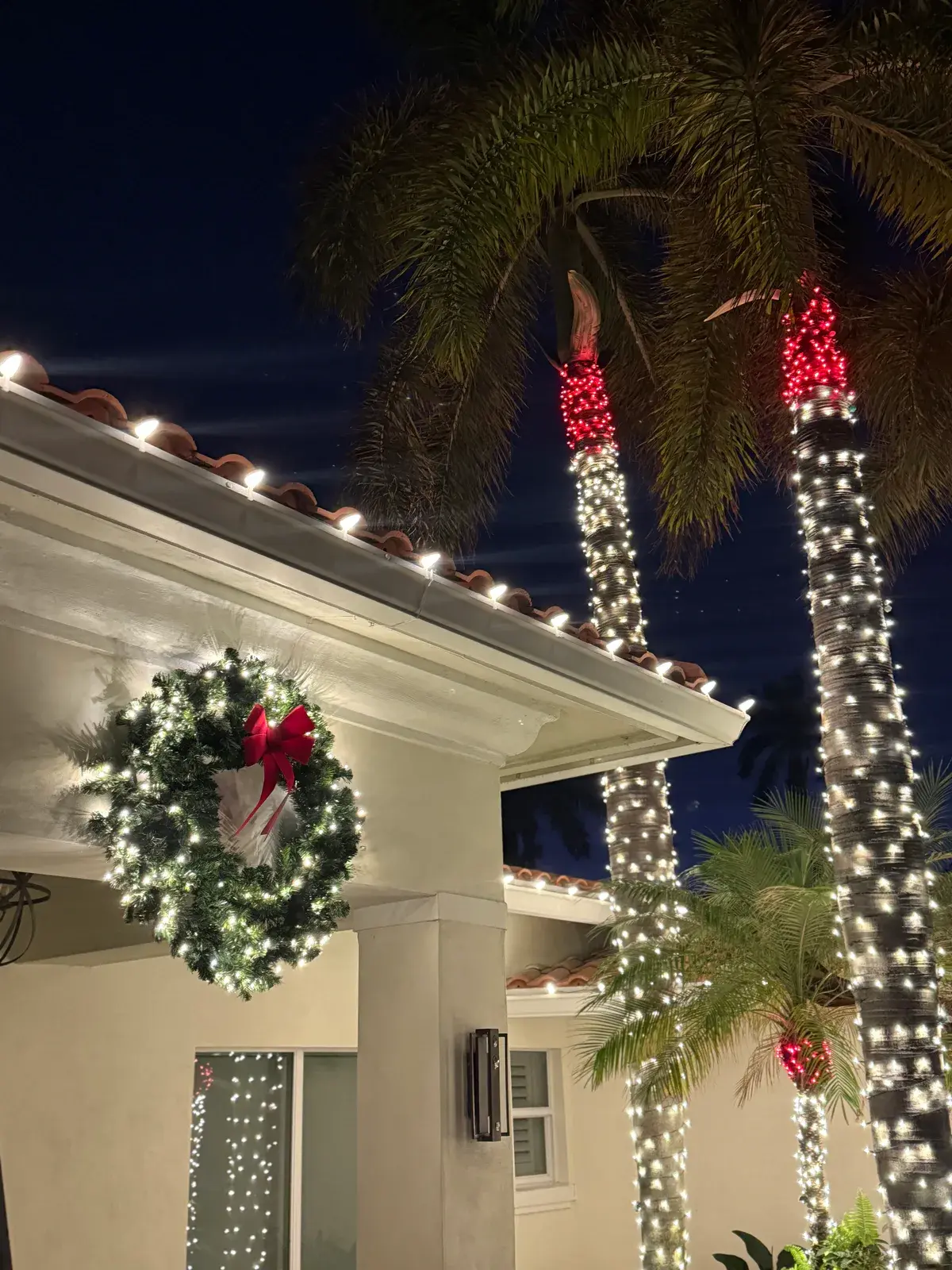 Close view of a lit holiday wreath and palm trees wrapped in red and warm white lights